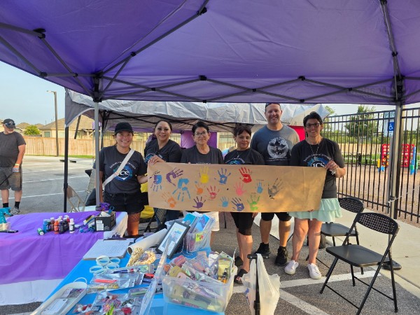 JCS team holding a colorful handprint banner under a purple tent